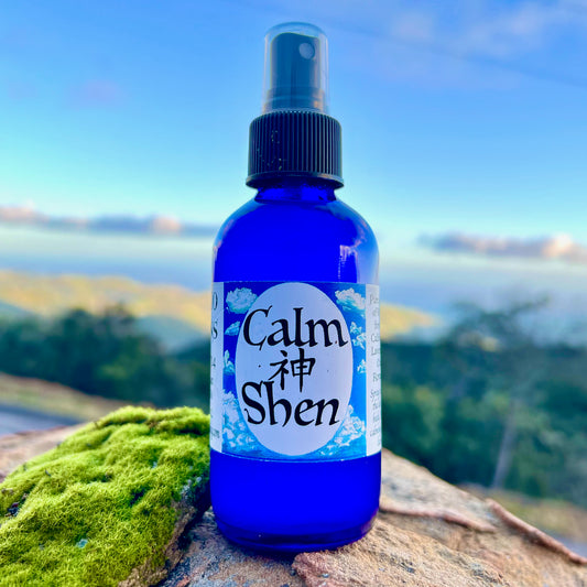 photograph of clam shen spray in cobalt blue bottle with on a rock with an ocean view in the back