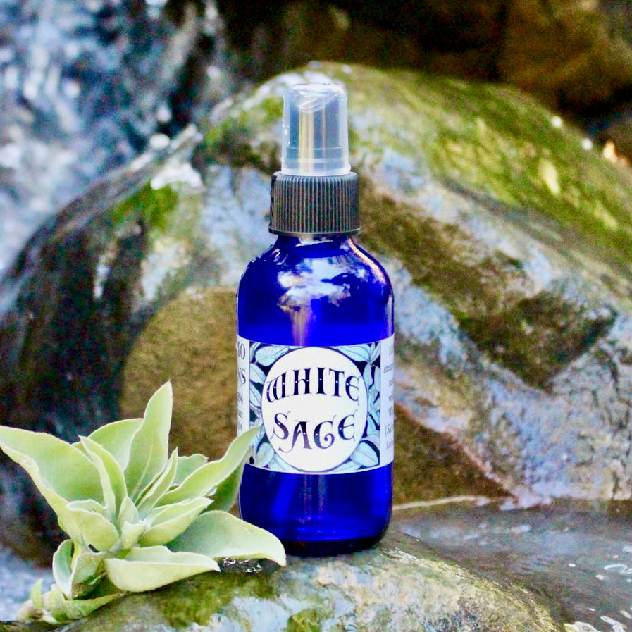 Photograph of a 4 oz cobalt blue glass spray bottle filled with White Sage hydrosol on rock with white sage leaves