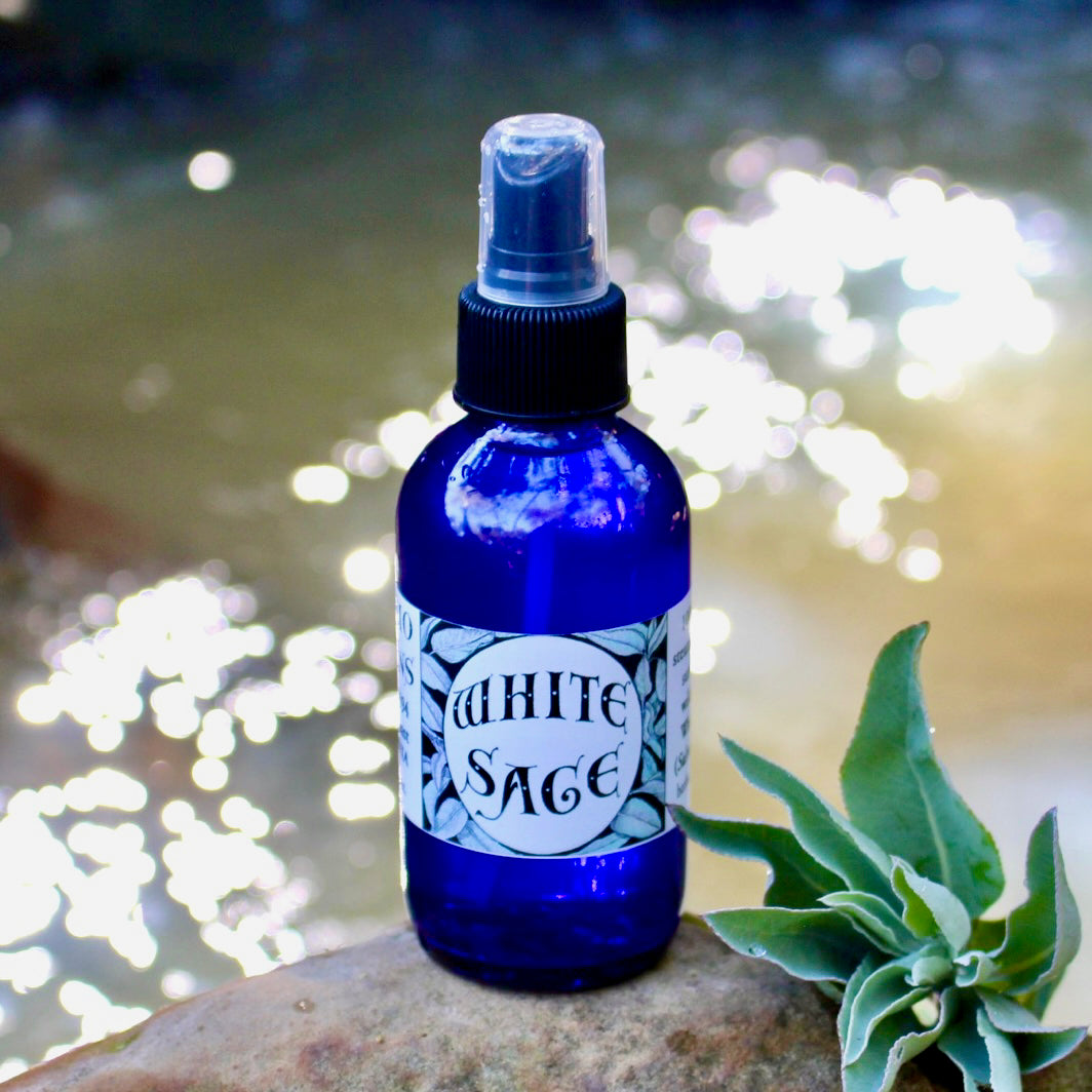 Photograph of a 4 oz cobalt blue glass spray bottle filled with White Sage hydrosol on rock with white sage leaves