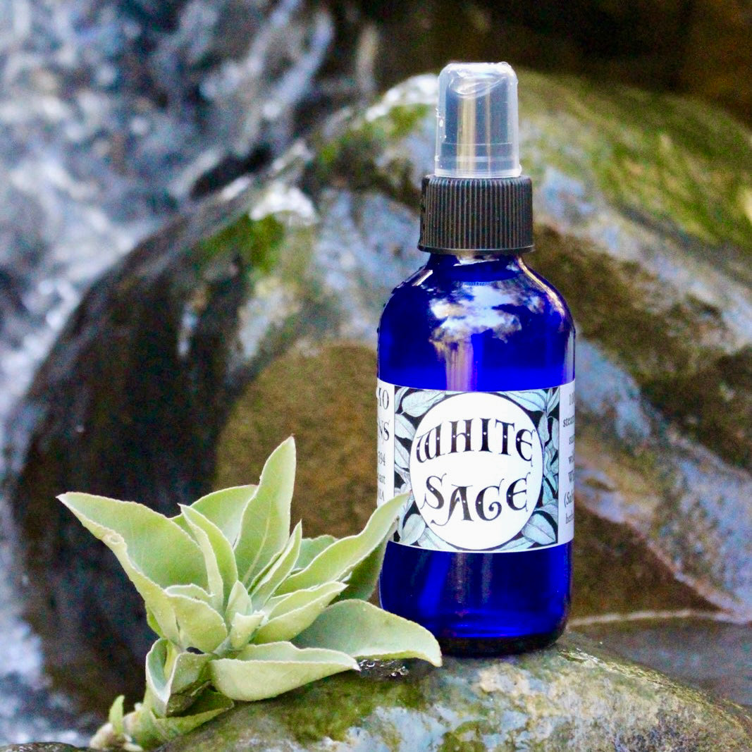 Photograph of a 4 oz cobalt blue glass spray bottle filled with White Sage hydrosol on rock with white sage leaves