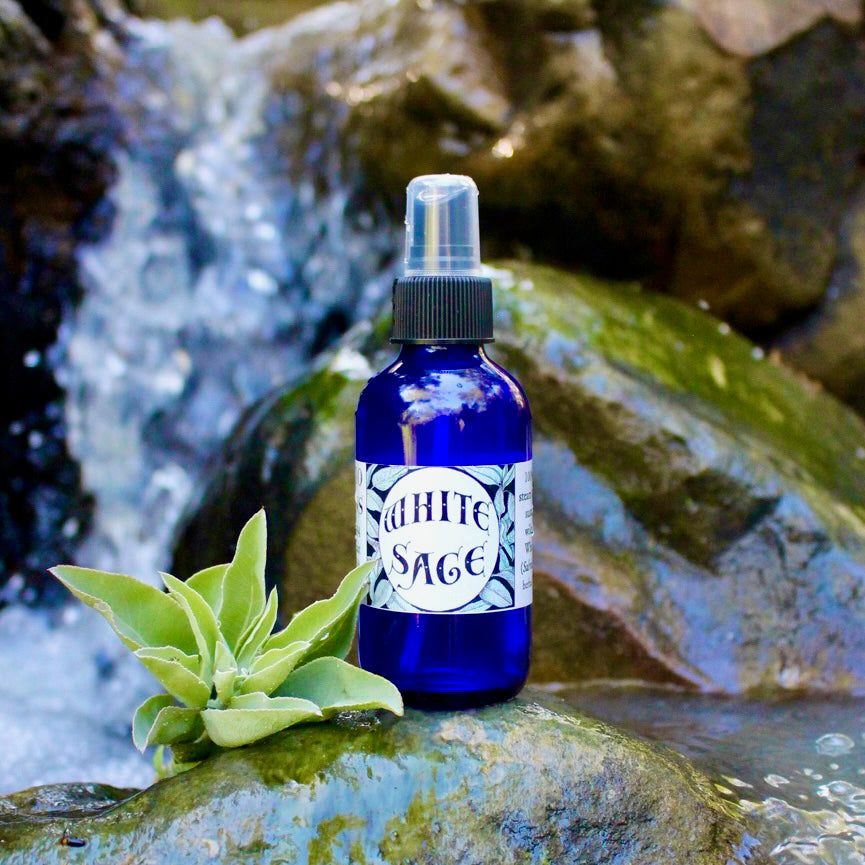 Photograph of a 4 oz cobalt blue glass spray bottle filled with White Sage hydrosol on rock with white sage leaves